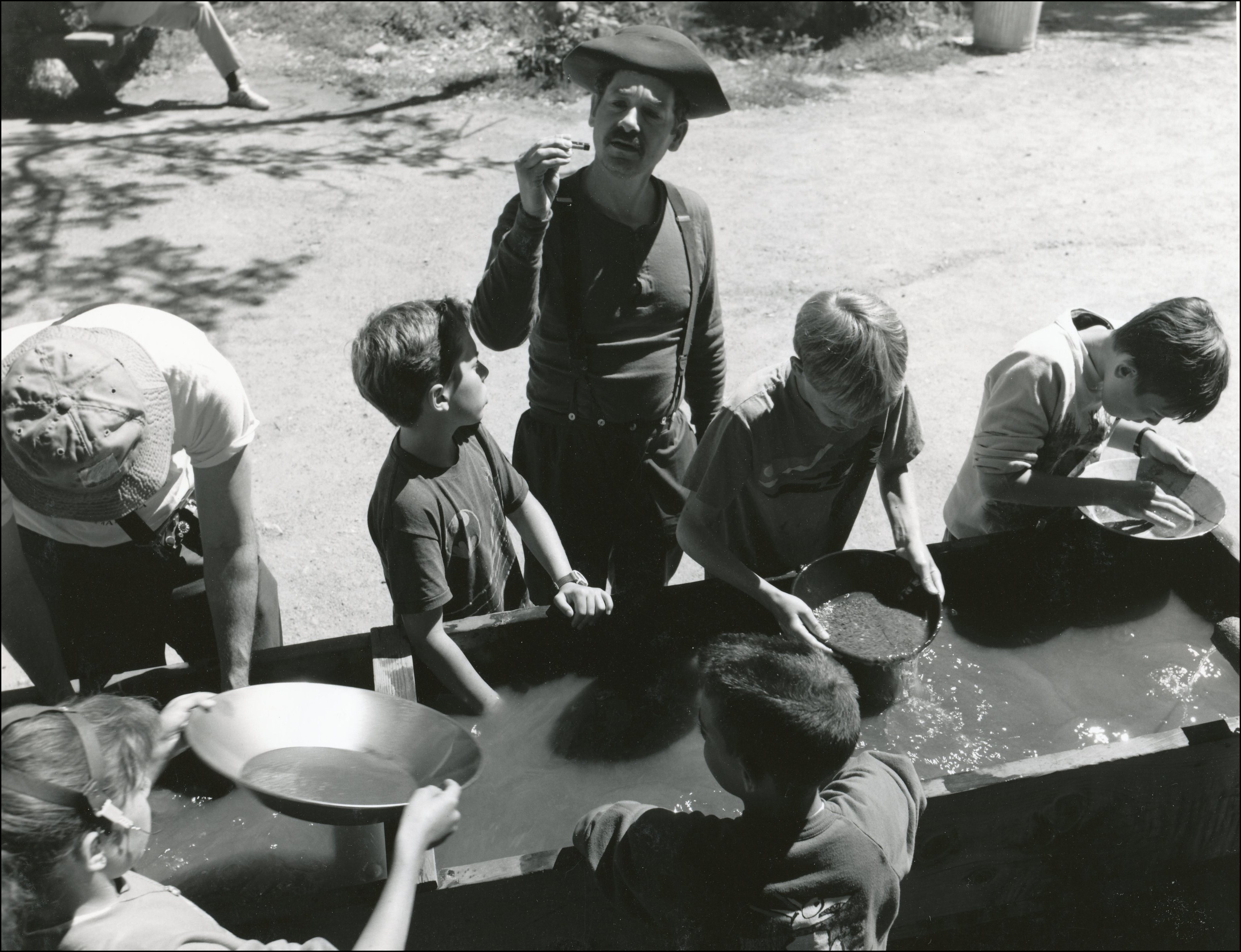 A group of kids around a long trough with water in it panning for gold.