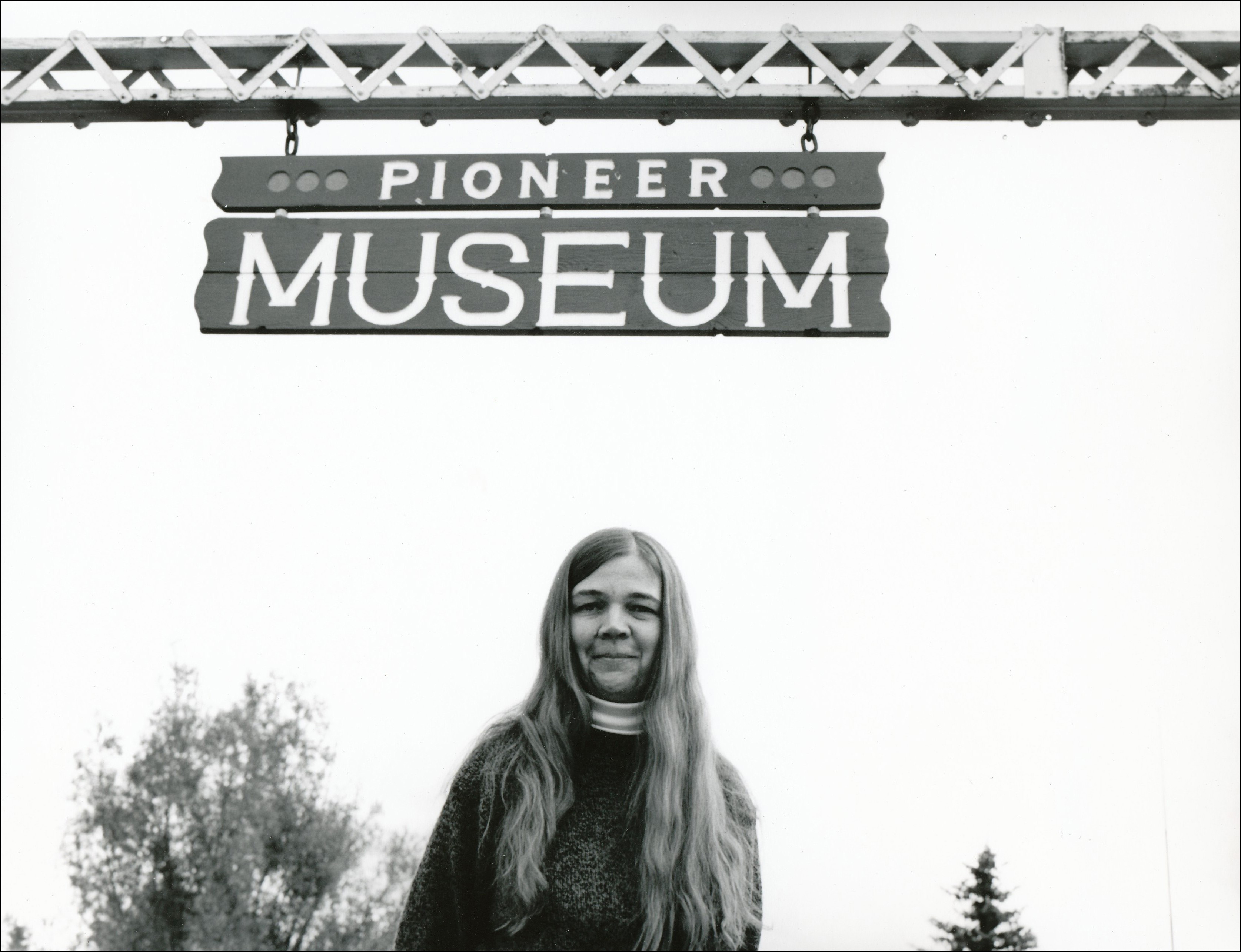 Woman with long hair standing under a sign that say Pioneer Museum