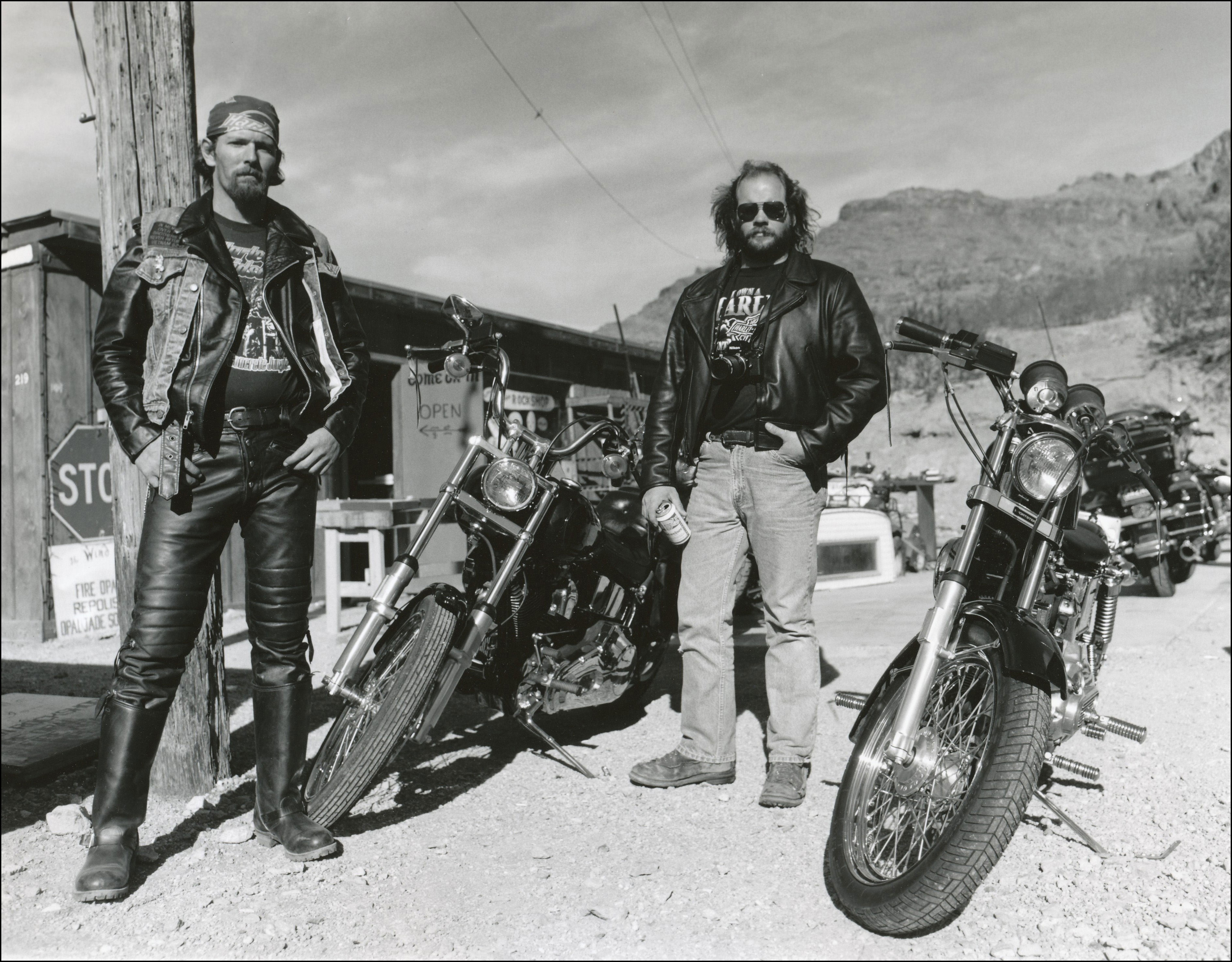 Motorcycle riders posing with their bikes in front of a small town gas station