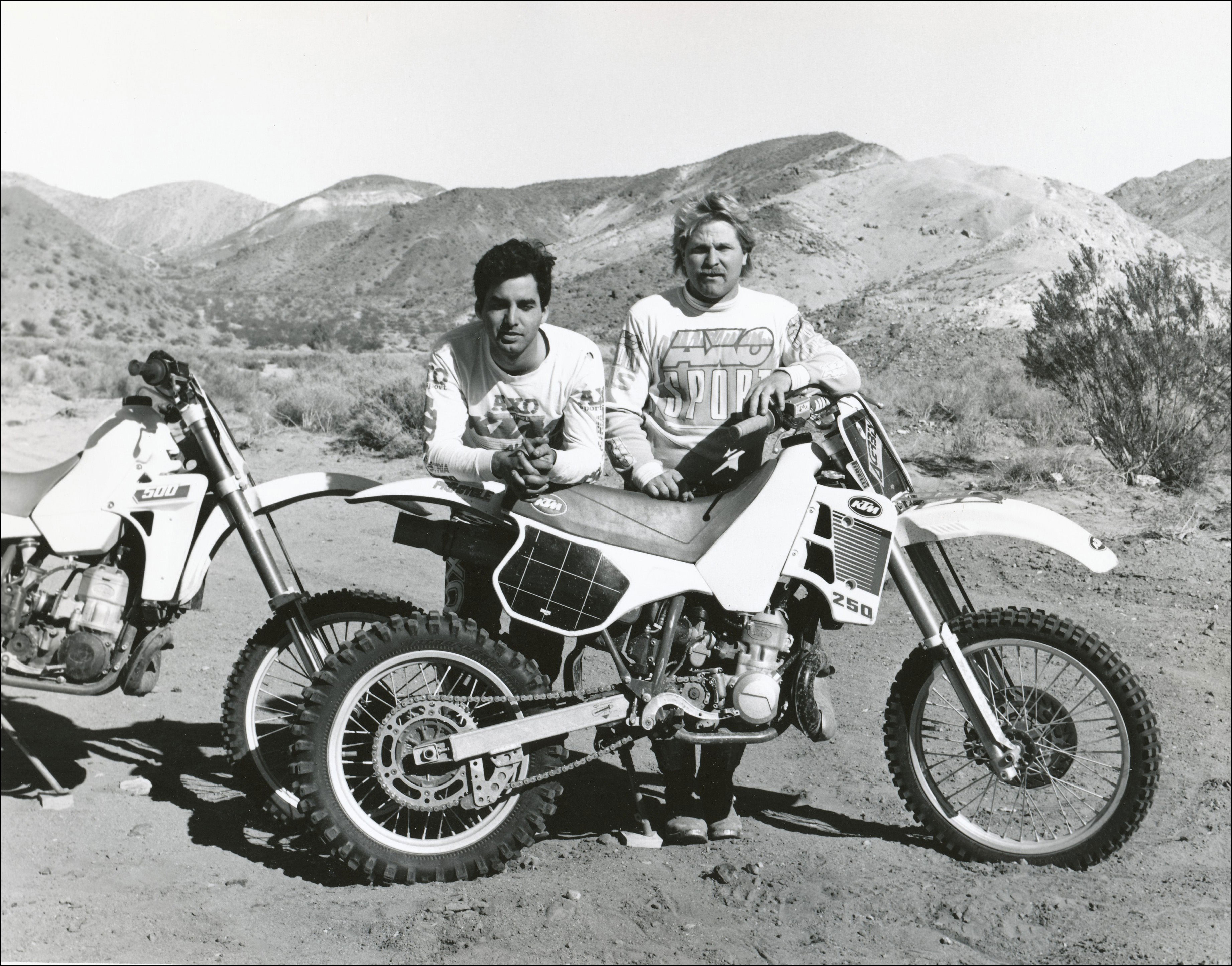 Dirt bikers posing with their bikes. Dry hills with sagebrush behind in the background