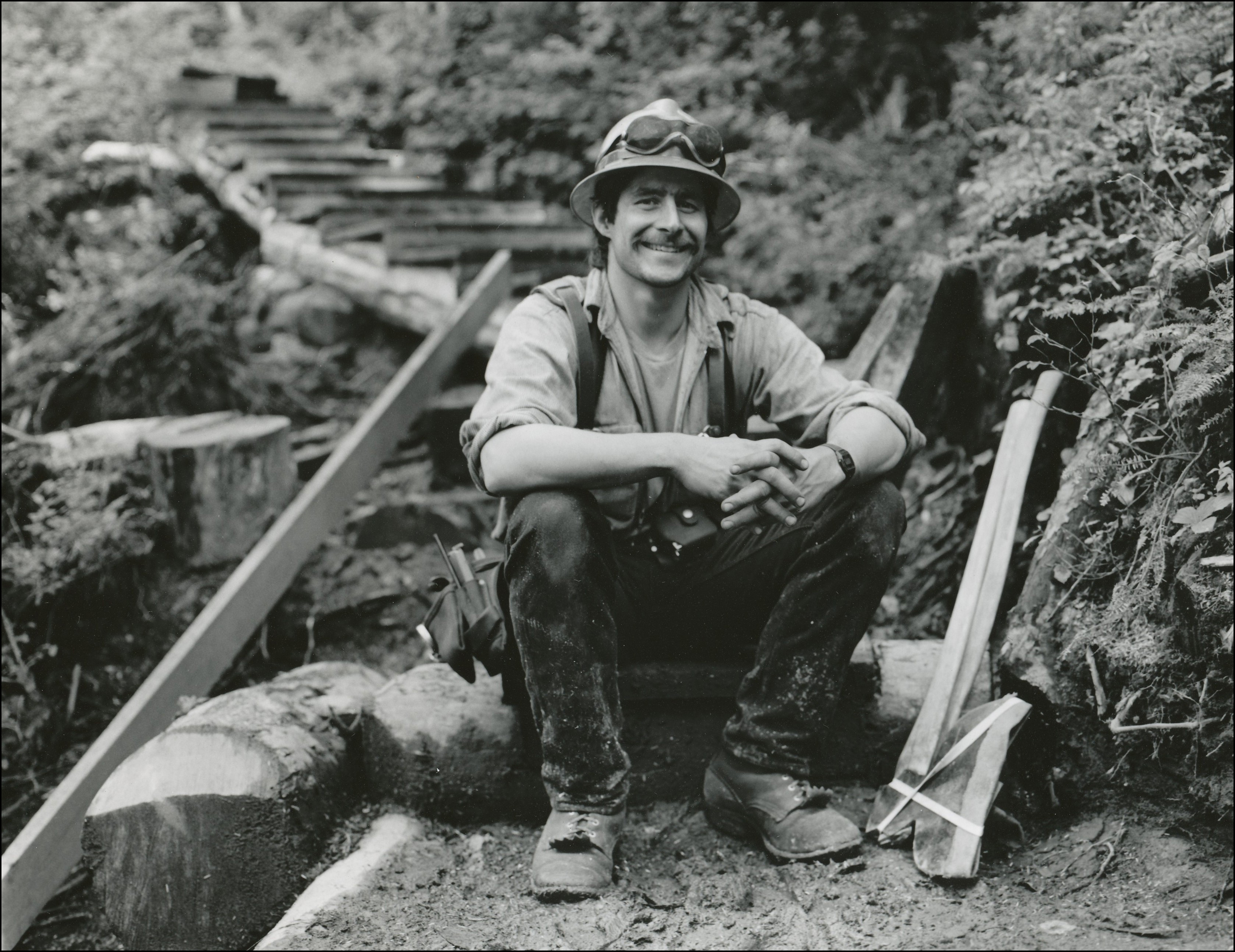 Miner with hard hat sitting on a step at the bottom of a trail smiling