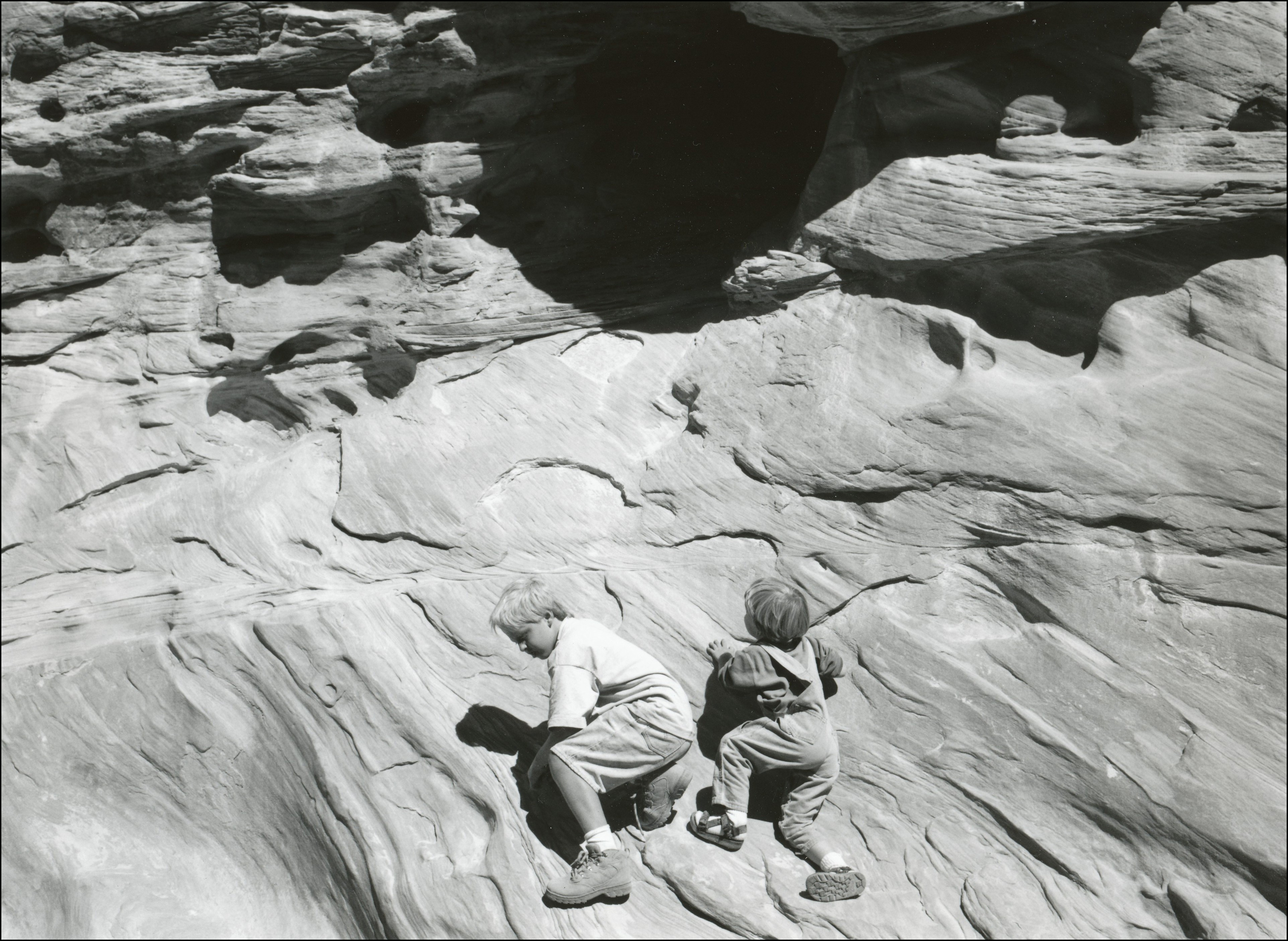 Two kids climbing up sandstone rock wall