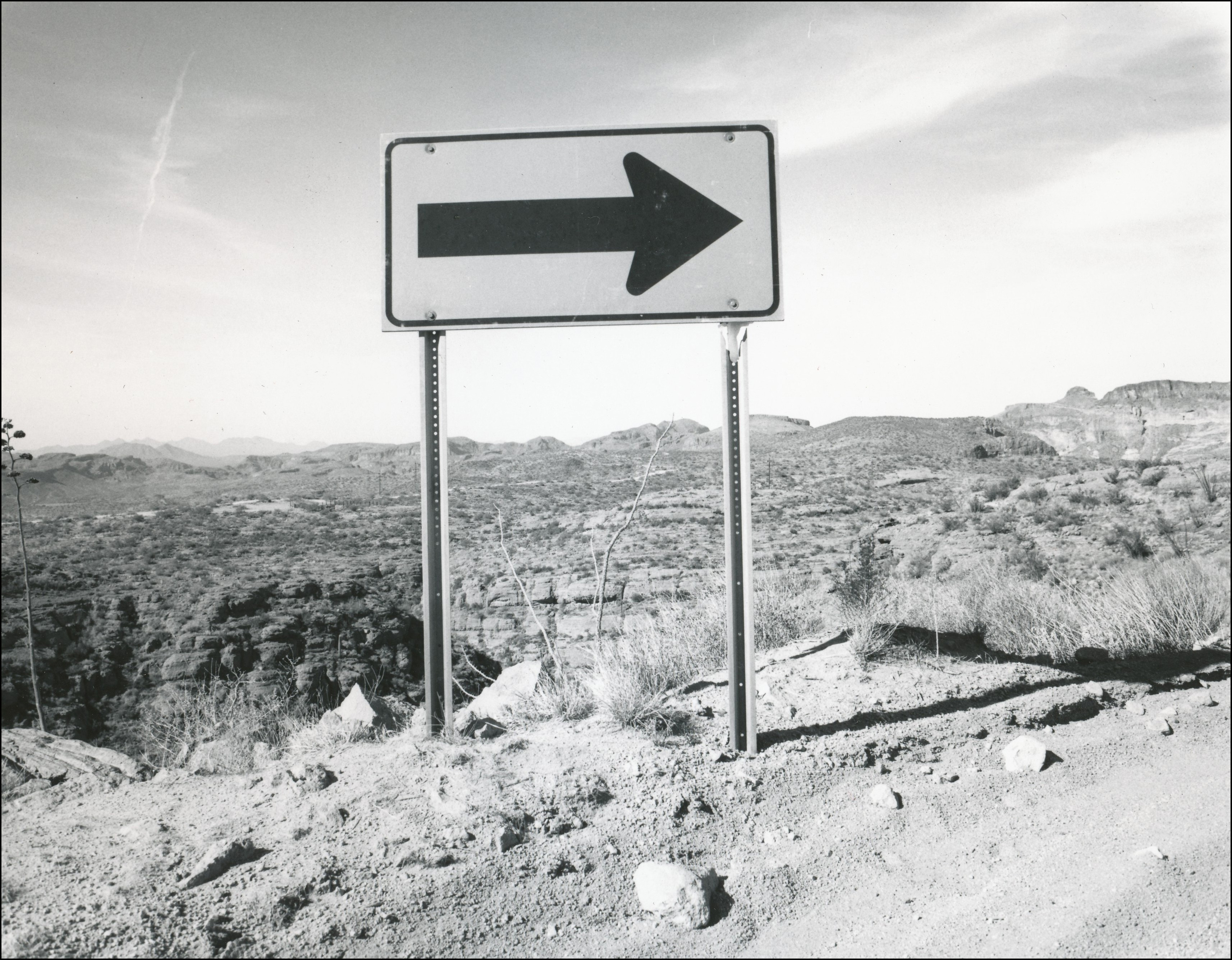Roadside arrow sign at edge of dirt road with steep dropoff
