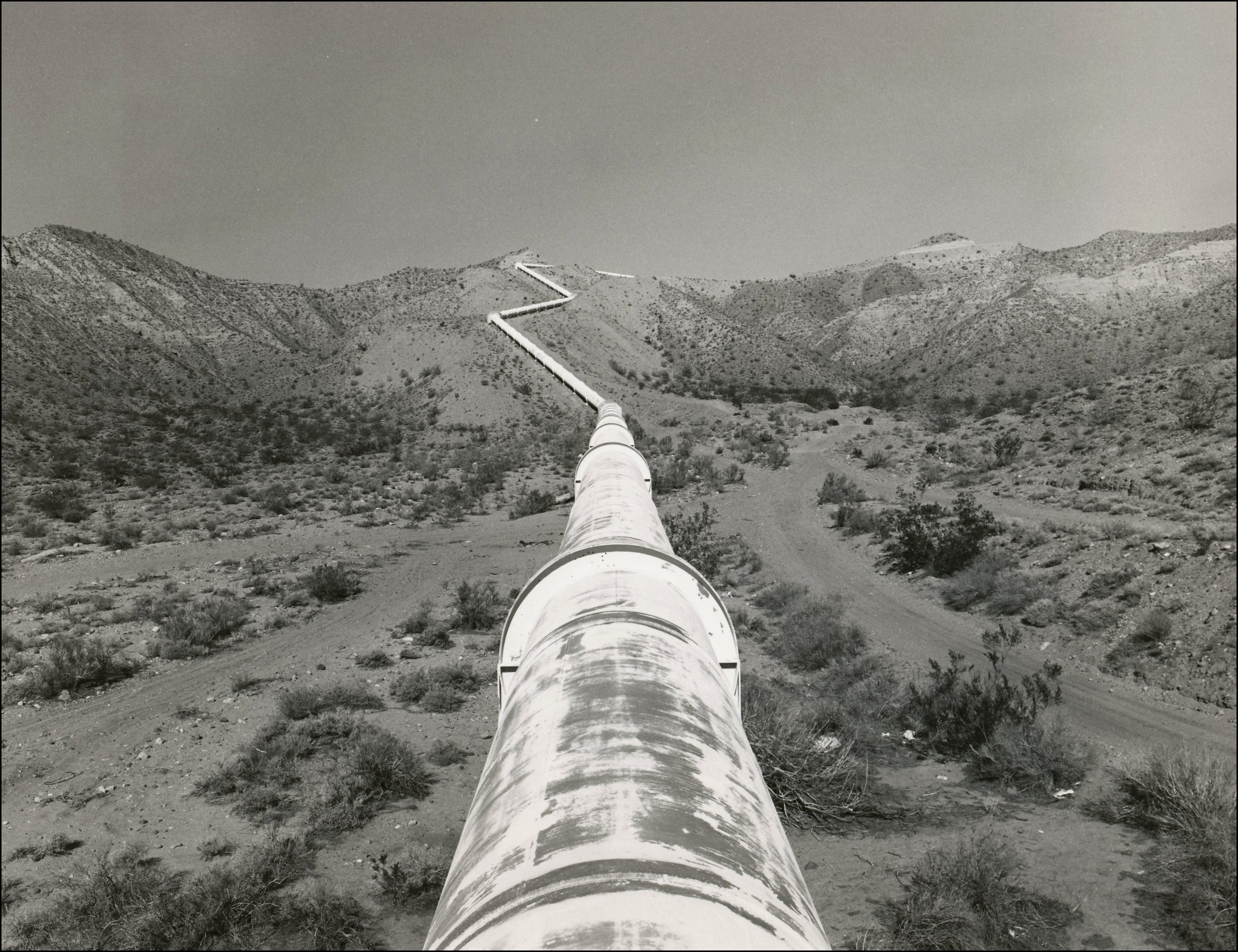 Looking down a large pipeline going through the desert and up over a hill
