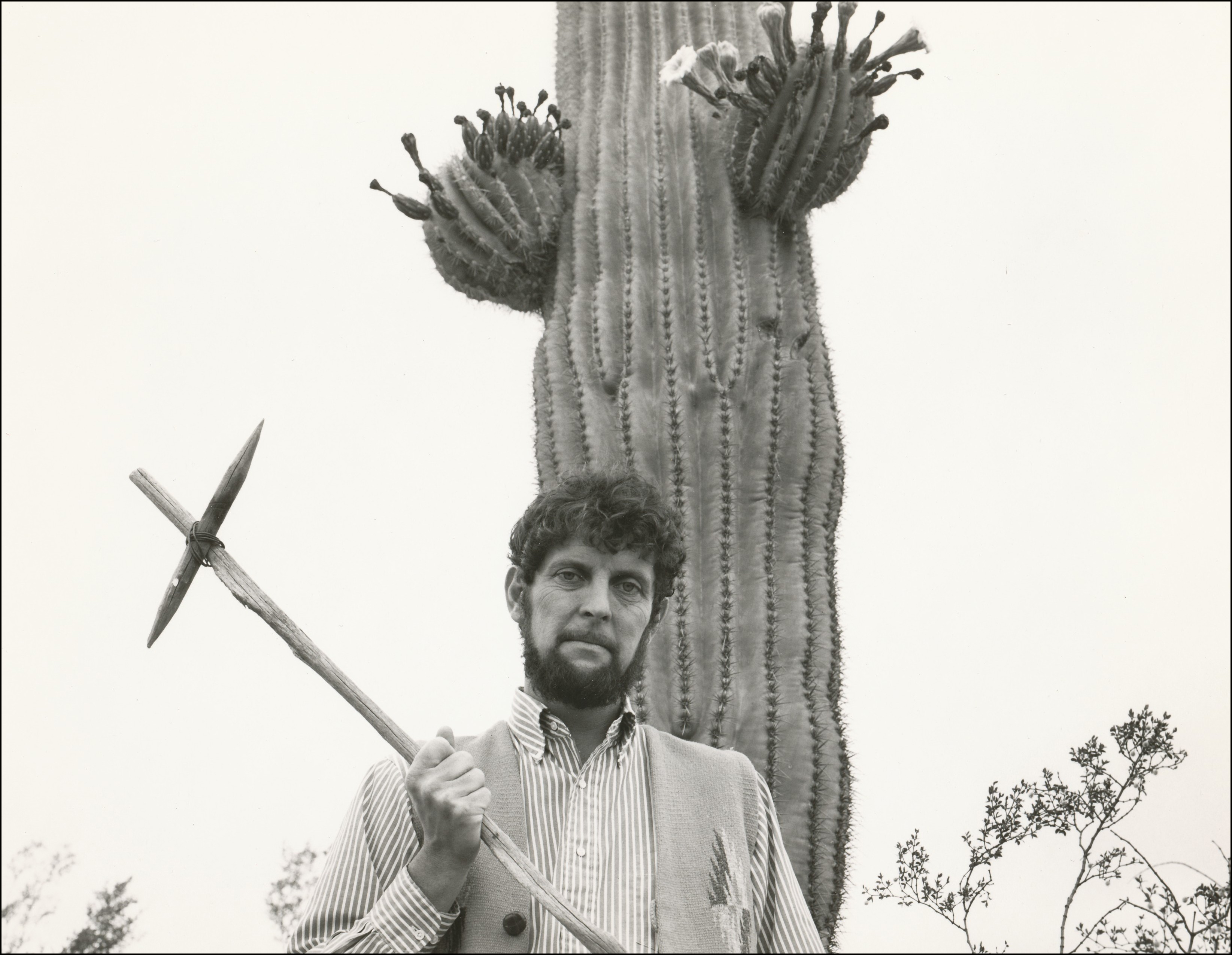 Man holding wooden cross standing in front of large saguaro cactus