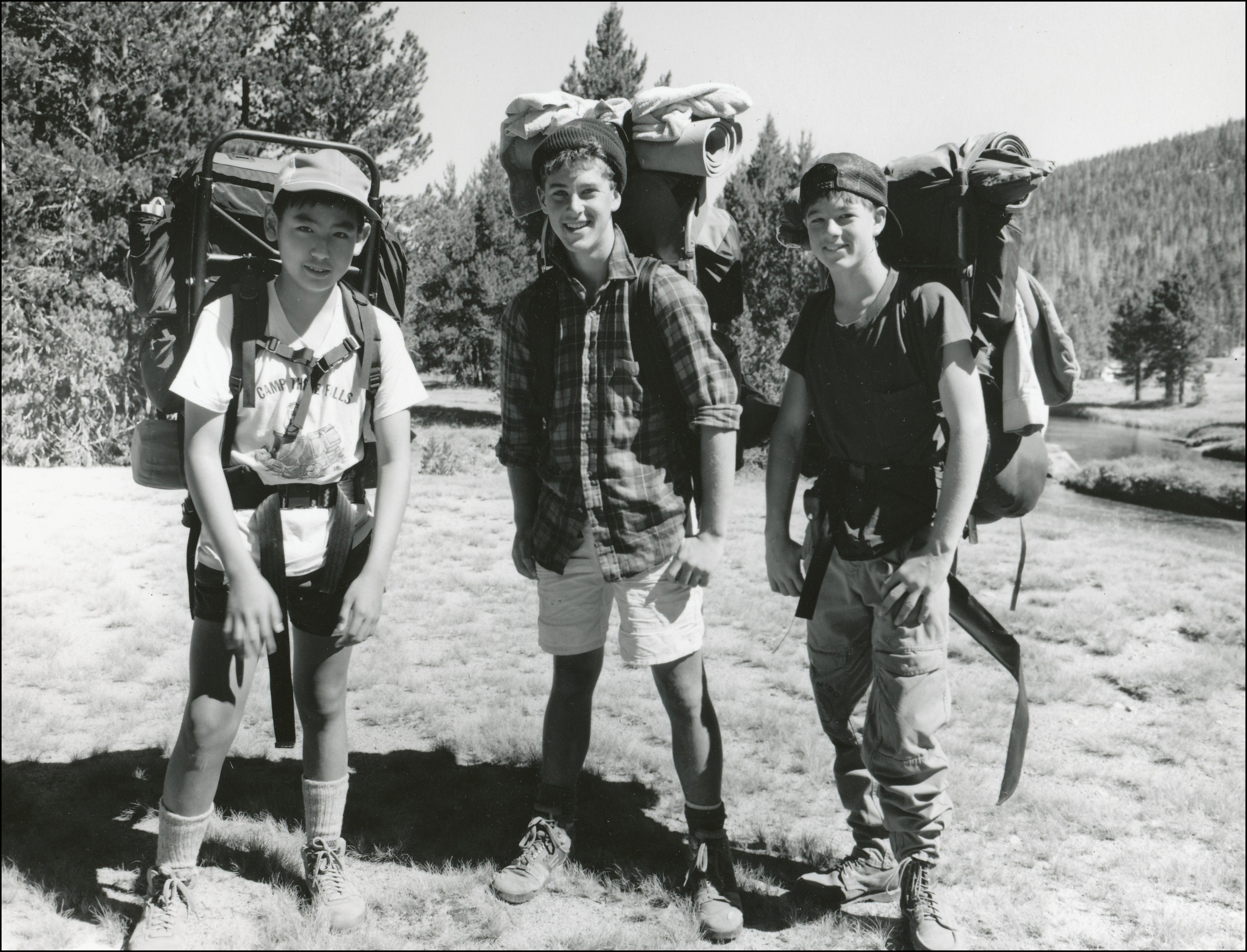 Three boy scouts posing in wilderness with large gear packs on their backs