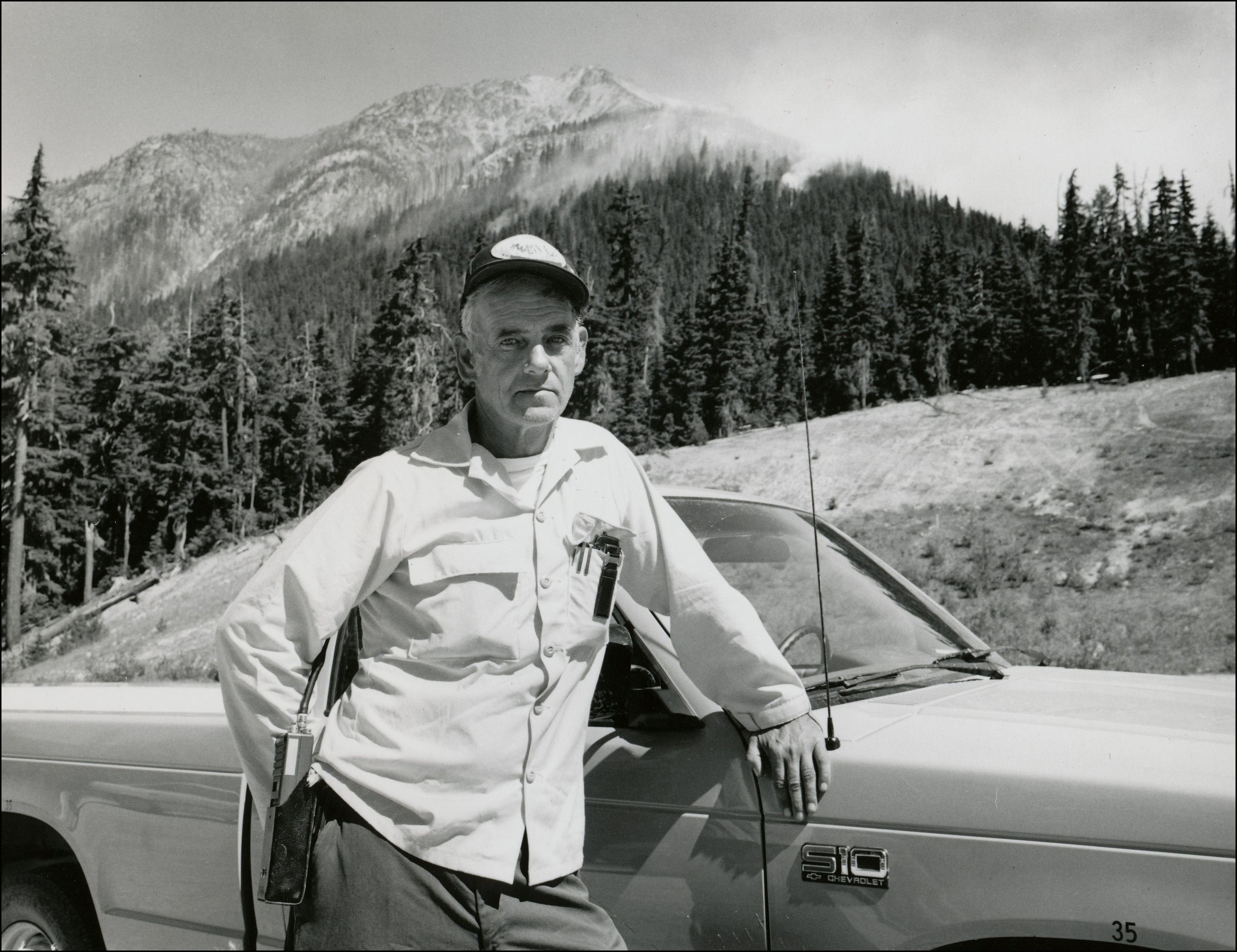 Man in baseball cap standing in front of his car with mountain in the background