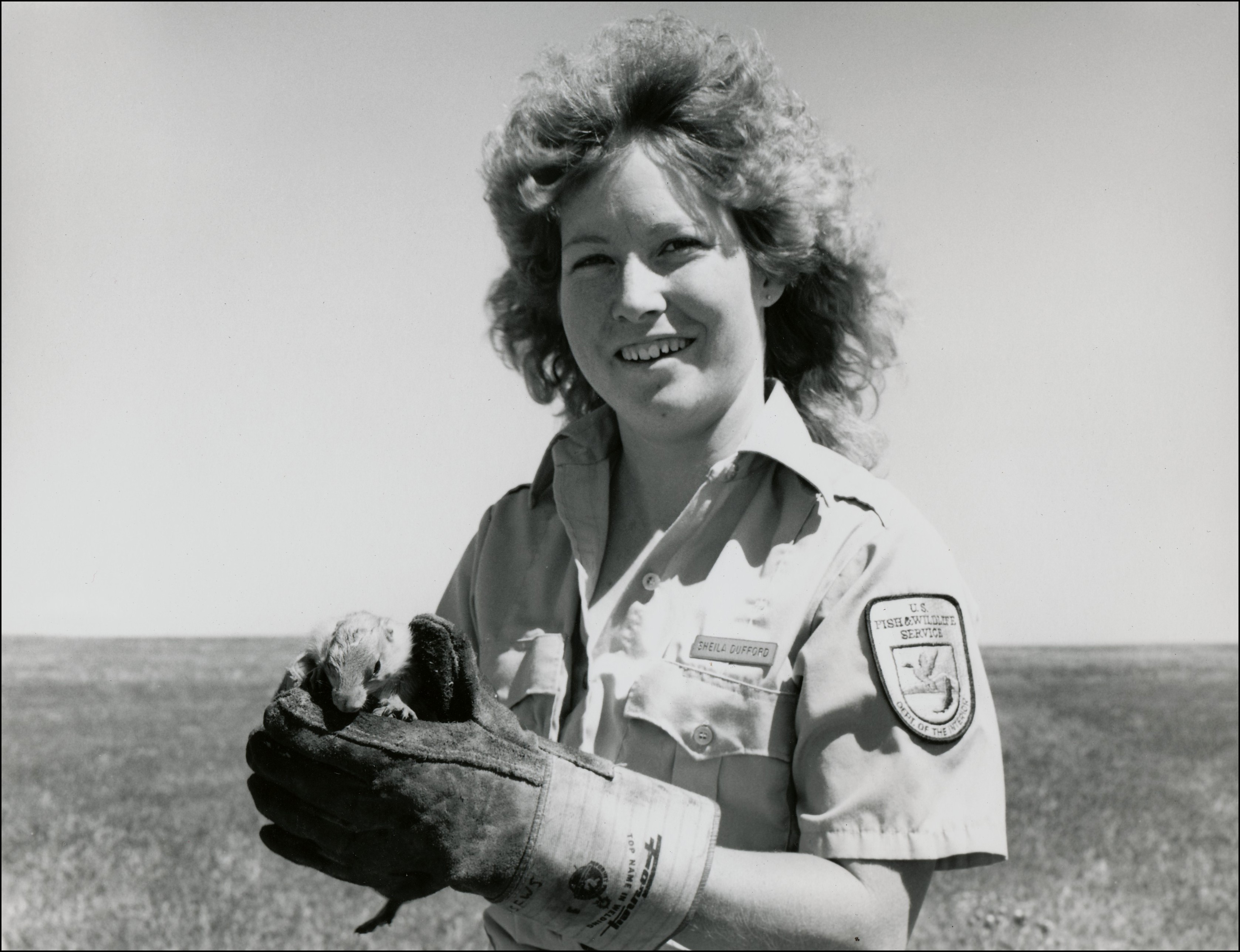 Woman in federal uniform with gloves on holding a prairie dog