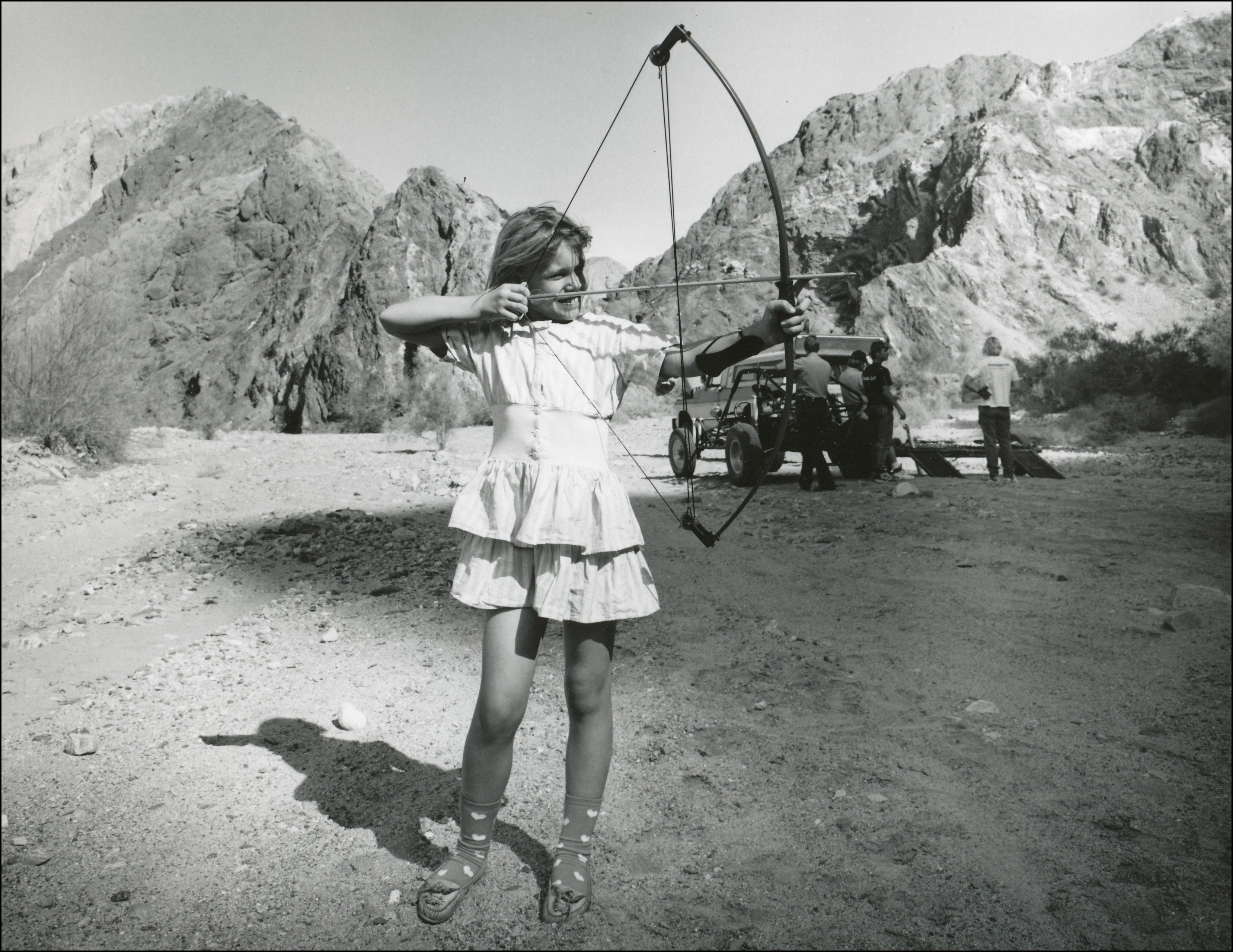 Young girl in dress aiming an old fashioned bow and arrow 